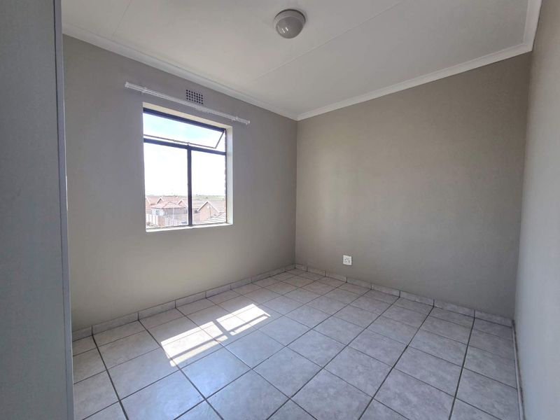 A clean, empty bedroom featuring neutral wall paint, tiled flooring, and a large window providing natural light.