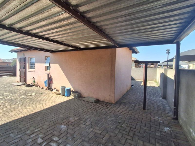 Rear exterior area featuring a paved courtyard, covered carport structure, and perimeter walling.