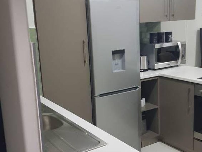 A modern kitchen featuring sleek grey cabinetry, white countertops, a stainless steel sink, and integrated appliances including an oven and microwave.