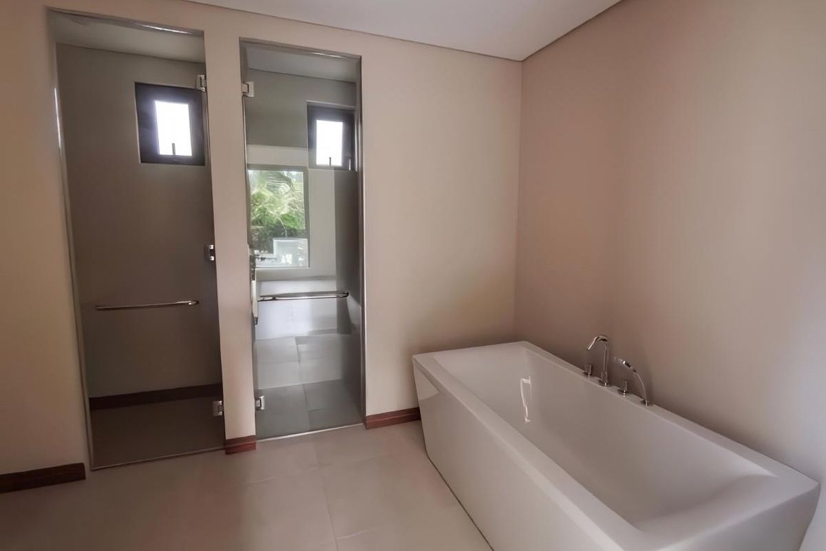 Modern bathroom featuring a sleek freestanding bathtub and separate glass-enclosed shower and toilet areas with neutral tiling.
