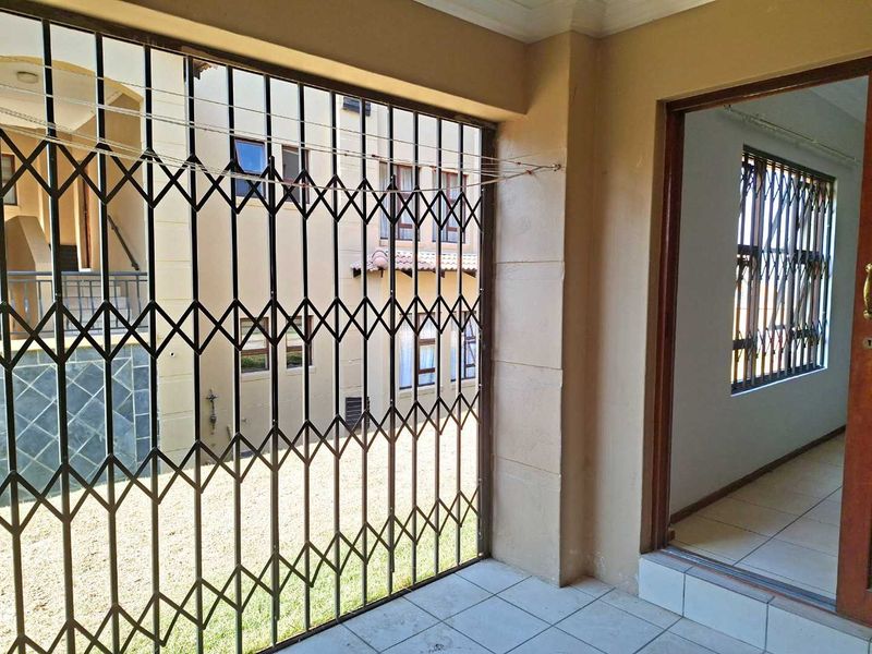 A covered patio area featuring tiled flooring and a metal security gate, providing access to the apartment interior.