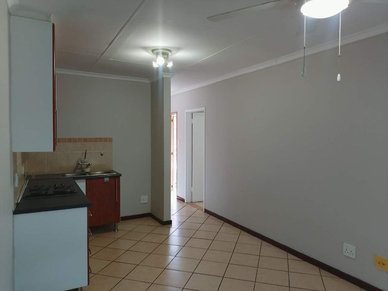 An open-plan kitchen and living area featuring tiled flooring, built-in cabinetry, and a functional hob, presenting a clean and versatile space.