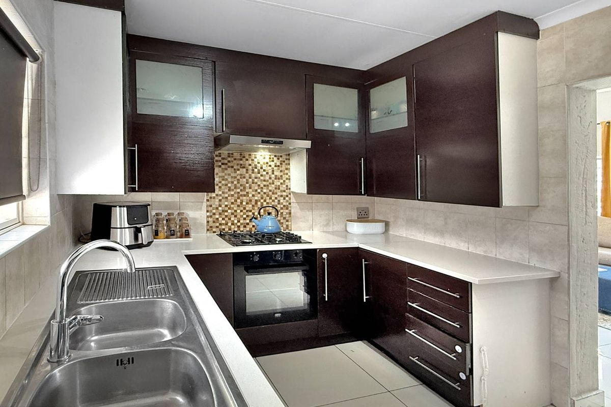 A functional kitchen featuring dark wood cabinetry, a built-in oven, gas hob, extractor fan, and a double stainless steel sink with tiled splashbacks.