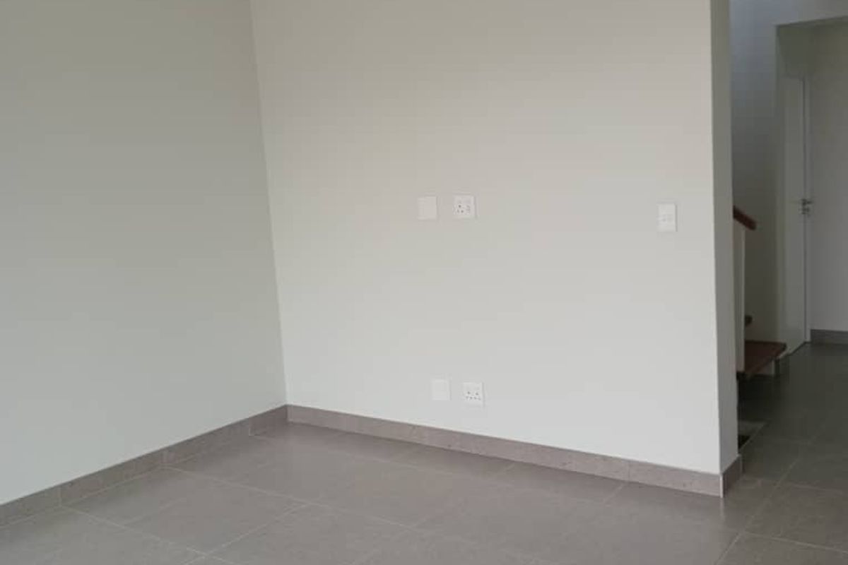 A bright, empty living area featuring neutral tiled flooring and recessed ceiling lighting, providing a clean and versatile space.