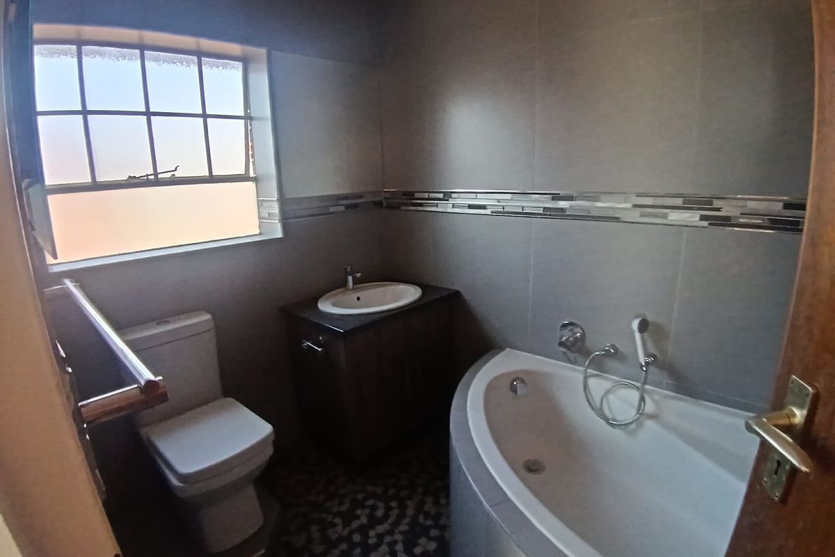 A modern bathroom featuring a corner bathtub, a vanity with a basin, a toilet, and tiled walls with a decorative mosaic border.