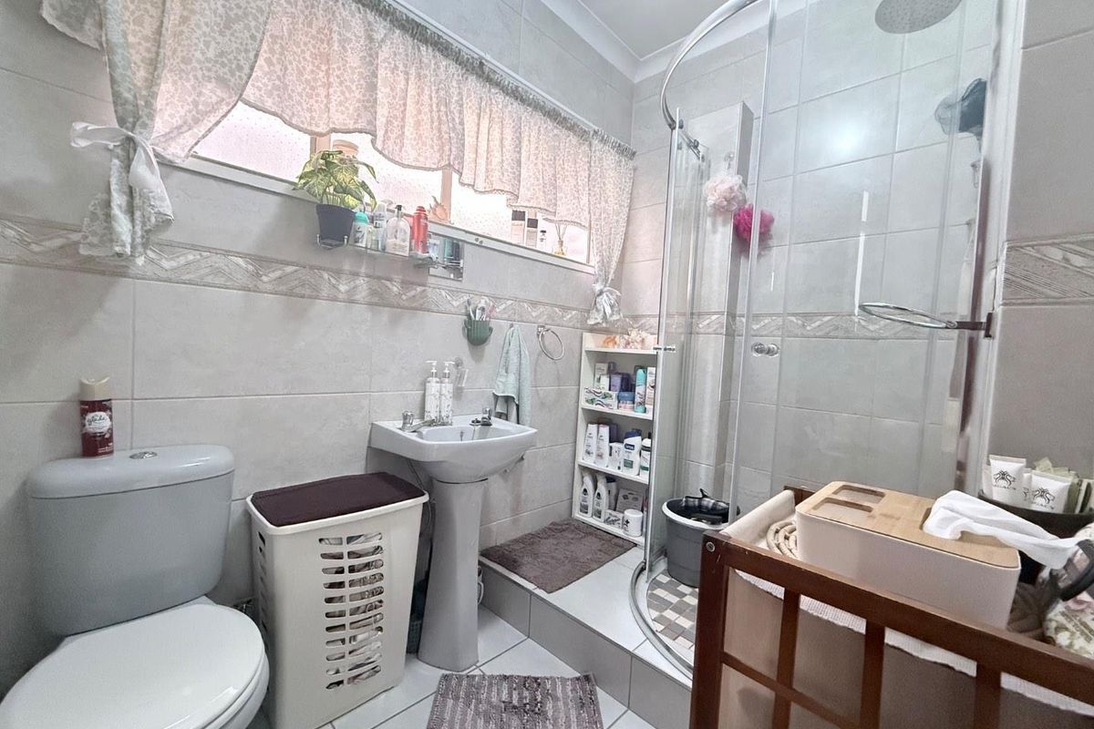 A functional bathroom featuring a pedestal sink, a glass-enclosed shower, and a standard toilet with neutral wall tiling.