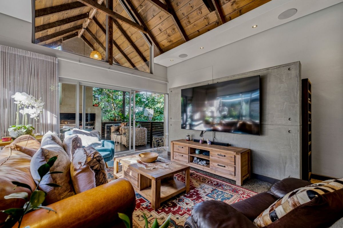 Spacious living room featuring a dramatic vaulted timber ceiling, exposed rafters, and a modern concrete feature wall with seamless indoor-outdoor flow.