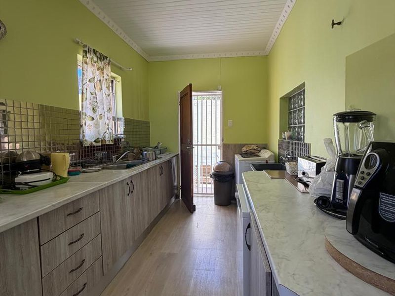 A functional galley-style kitchen featuring laminate cabinetry, marble-effect countertops, tiled backsplash, and direct access to the exterior via a security gate.