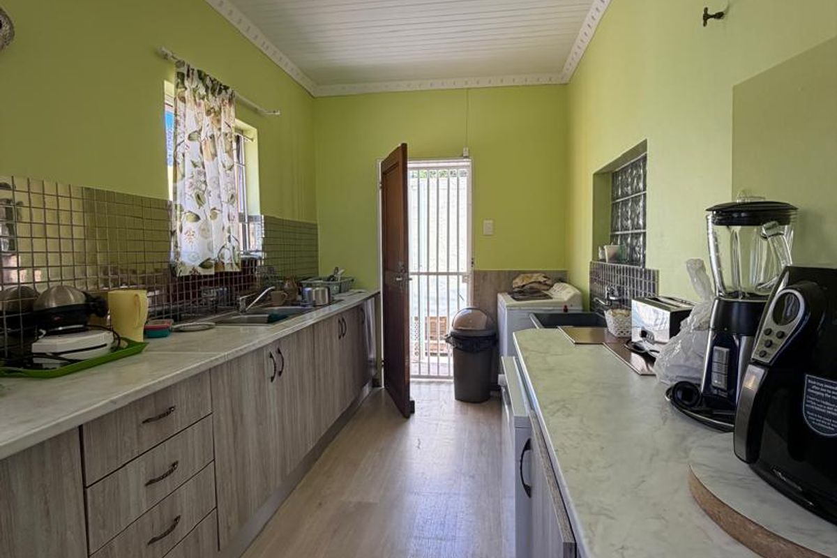 A functional galley-style kitchen featuring laminate cabinetry, marble-effect countertops, tiled backsplash, and direct access to the exterior via a security gate.