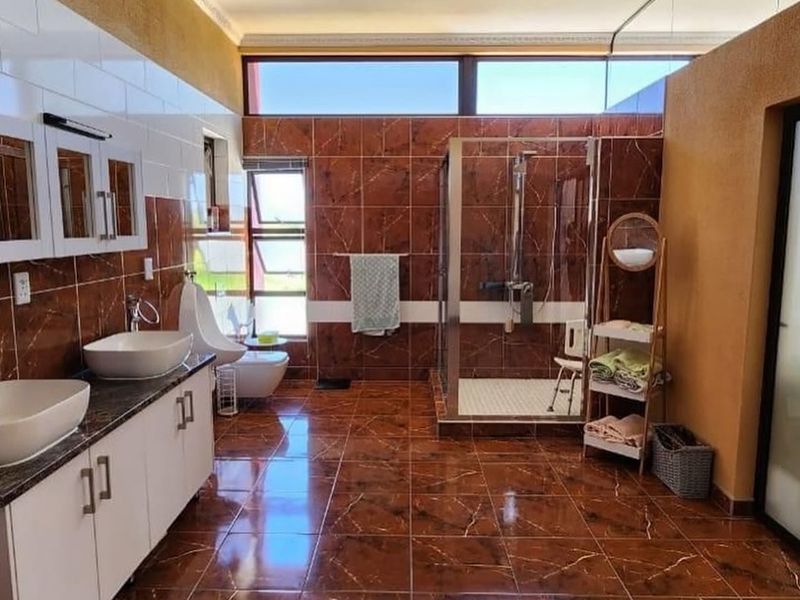 Spacious bathroom featuring a double vanity with vessel sinks, a walk-in shower with glass enclosure, toilet, bidet, and high-gloss tiled finishes.