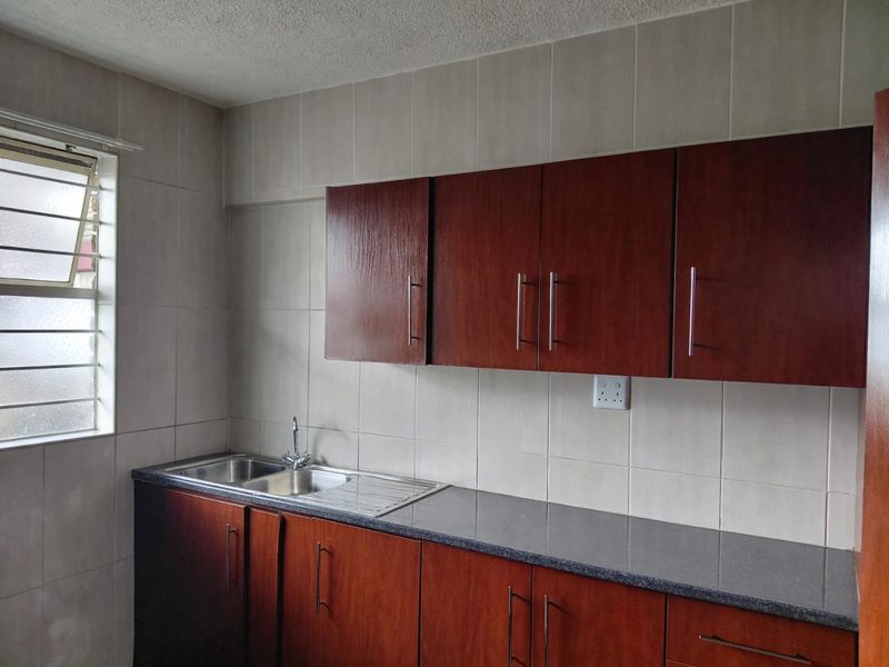 A functional kitchen area featuring dark wood-finish cabinetry, a stainless steel double sink, and neutral wall tiling.