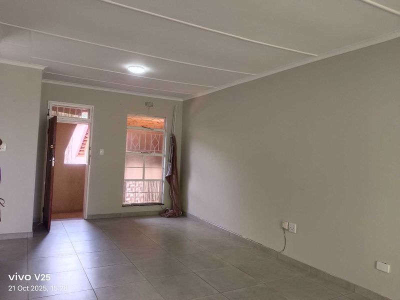 An empty living area featuring tiled flooring, ceiling panels, and direct access to an exterior space through a security gate.
