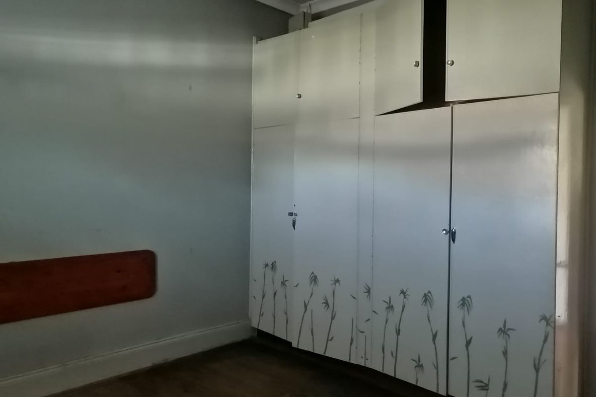 A bedroom featuring built-in cupboards with decorative detailing, requiring some maintenance and cosmetic updates to restore its appeal.