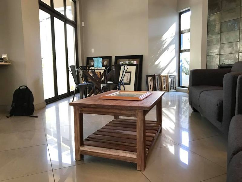 A bright and spacious living area featuring large glass sliding doors, expansive windows, and polished tiled flooring with a modern feature wall.