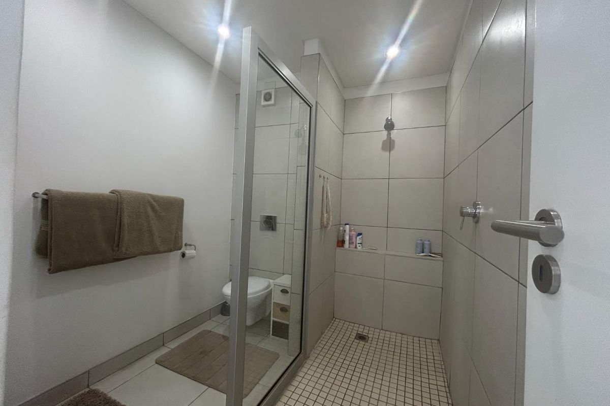 Modern bathroom featuring a spacious walk-in shower with glass screen, wall-mounted toilet, and neutral floor-to-ceiling tiling.