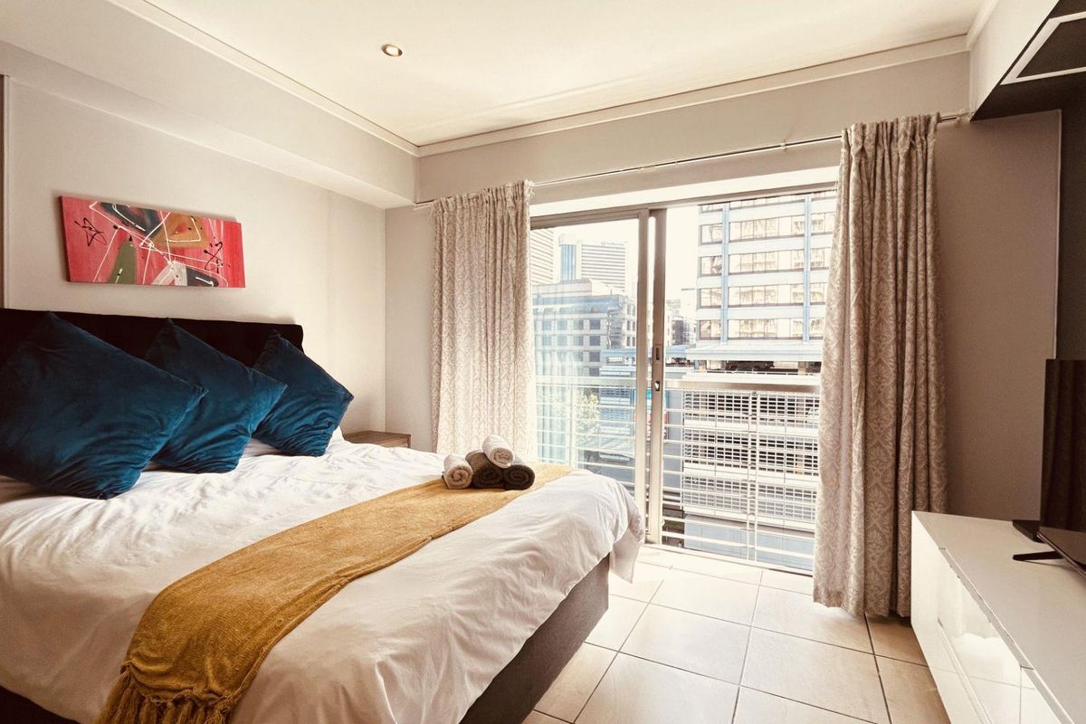 A well-lit bedroom featuring tiled flooring and a large sliding glass door that provides access to a balcony with city views.