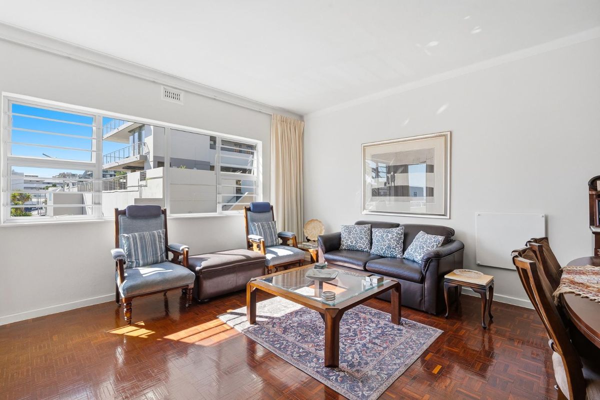 A bright living room featuring polished parquet flooring, large windows providing natural light, and classic cornice detailing.