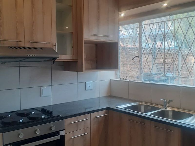 A functional kitchen featuring light wood-finish cabinetry, granite countertops, a stainless steel double sink, and built-in cooking appliances with a tiled backsplash.