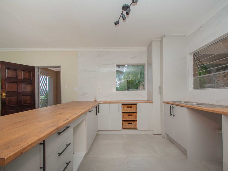Modern kitchen featuring light grey cabinetry, warm wooden countertops, marble-look splashback tiles, and a functional double sink layout.