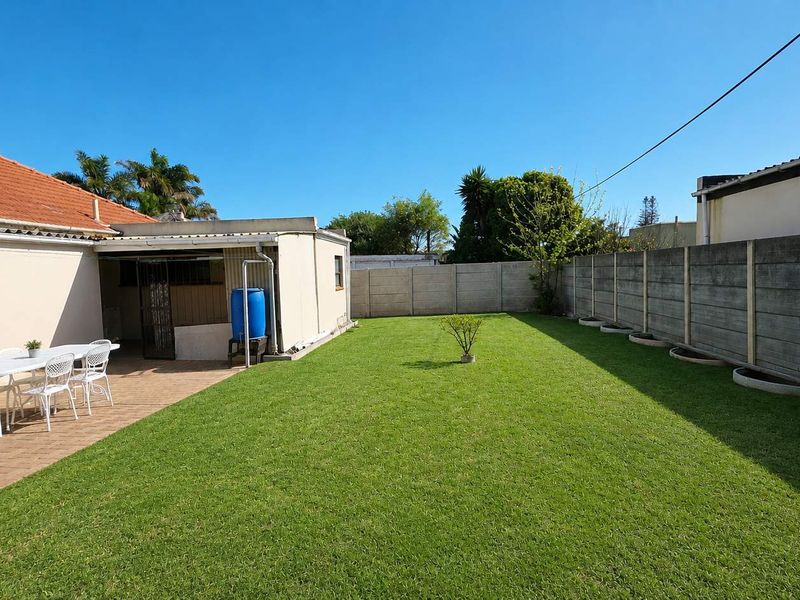 A spacious rear garden featuring a paved patio area, well-maintained lawn, and secure precast concrete boundary walling.