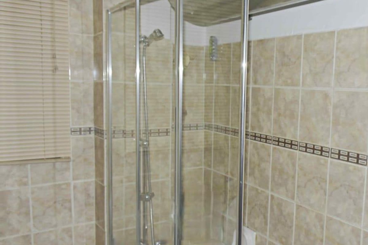 A bathroom featuring a shower-over-bath combination with tiled walls and a window with fitted blinds.
