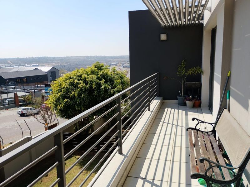 A spacious balcony featuring tiled flooring, a modern metal balustrade, and a slatted pergola, offering elevated views of the surrounding area.