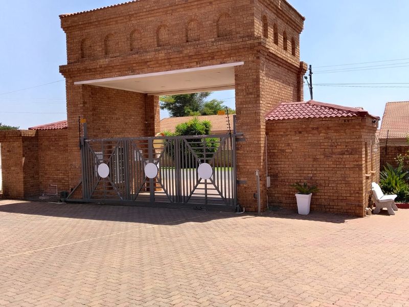 A secure gated entrance to the townhouse complex featuring a brick gatehouse, electric sliding gate, and paved driveway.