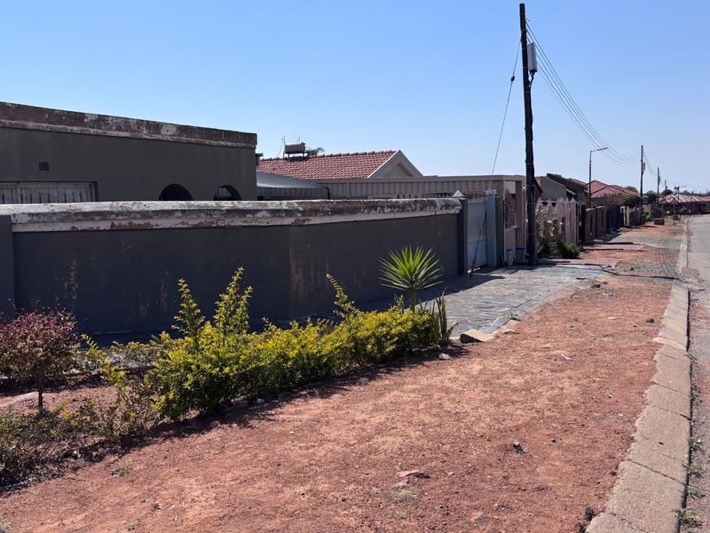Street view showing the property boundary wall, paved walkway, and surrounding neighbourhood infrastructure.