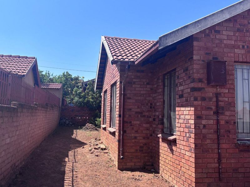 A side view of a face brick house featuring a tiled roof, security bars on windows, and a surrounding boundary wall.