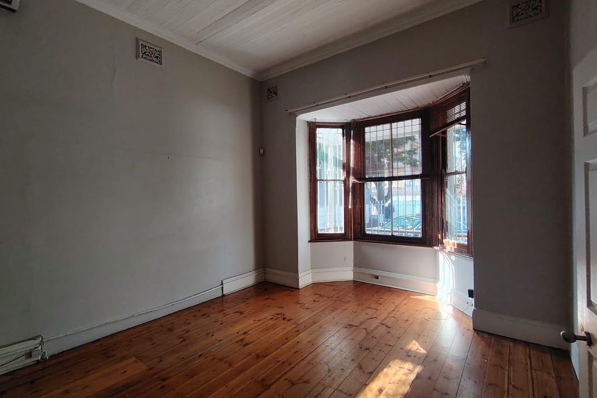 An empty office space featuring polished timber flooring, a classic bay window, and neutral wall tones, providing a versatile workspace.