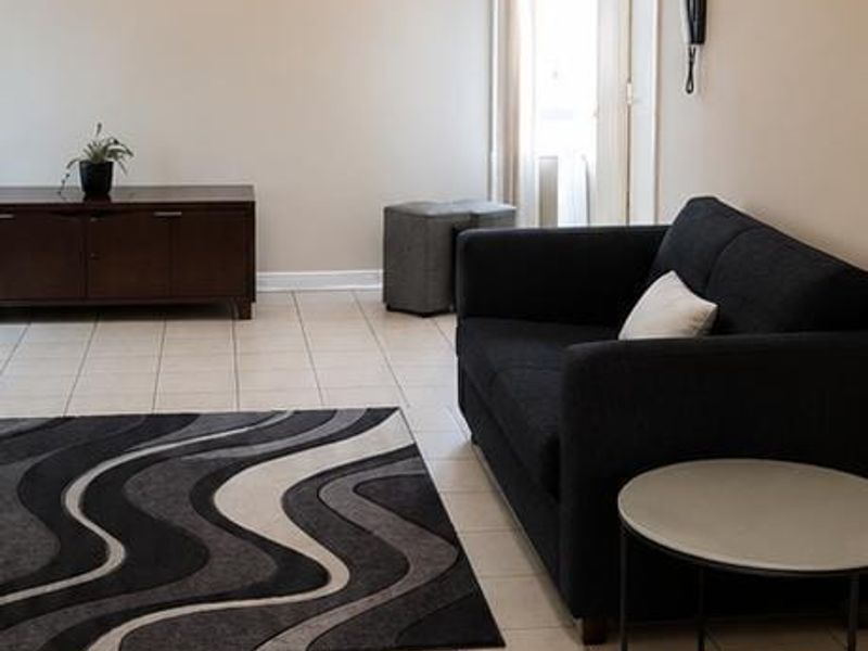 A neutrally painted living room featuring tiled flooring, a central ceiling light fixture, and a wall-mounted intercom system.