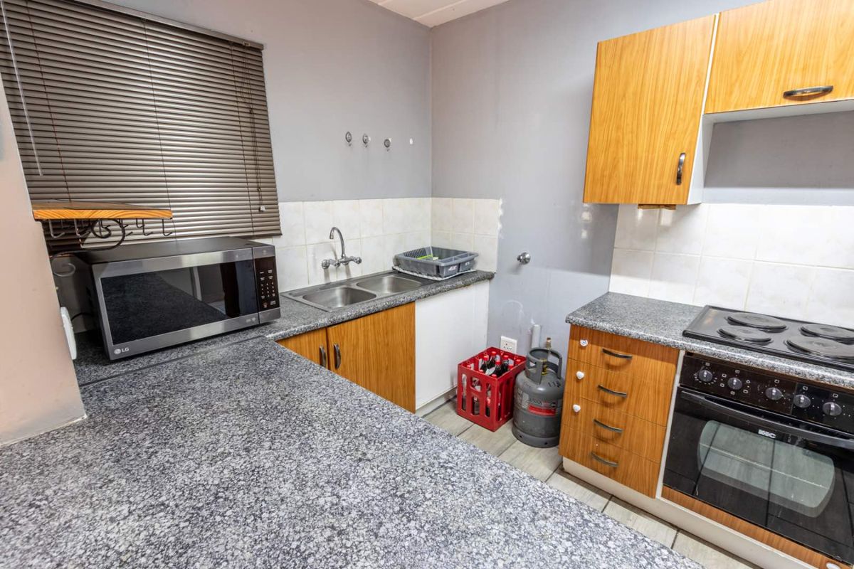 A functional kitchen featuring granite countertops, wood-finish cabinetry, a built-in oven with electric hob, and a double-basin sink.