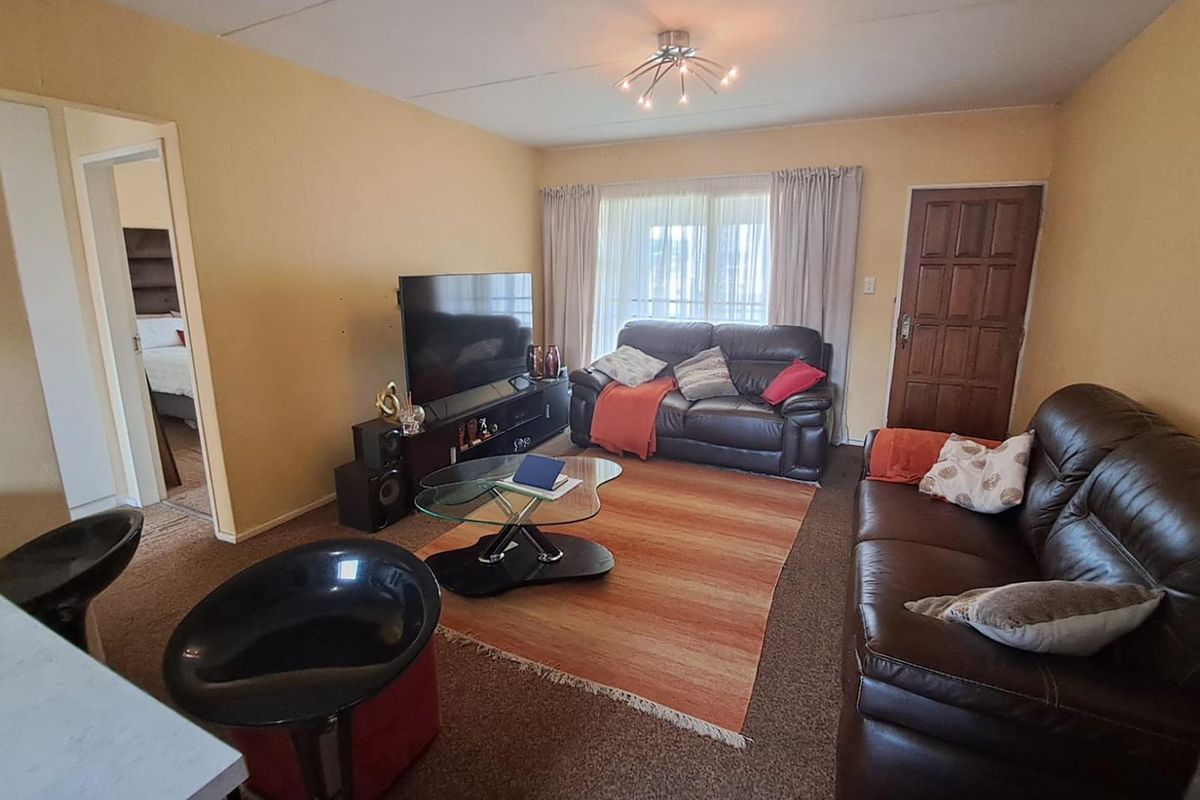 A living room area featuring carpet flooring, a central ceiling light fixture, and access to an adjacent bedroom.