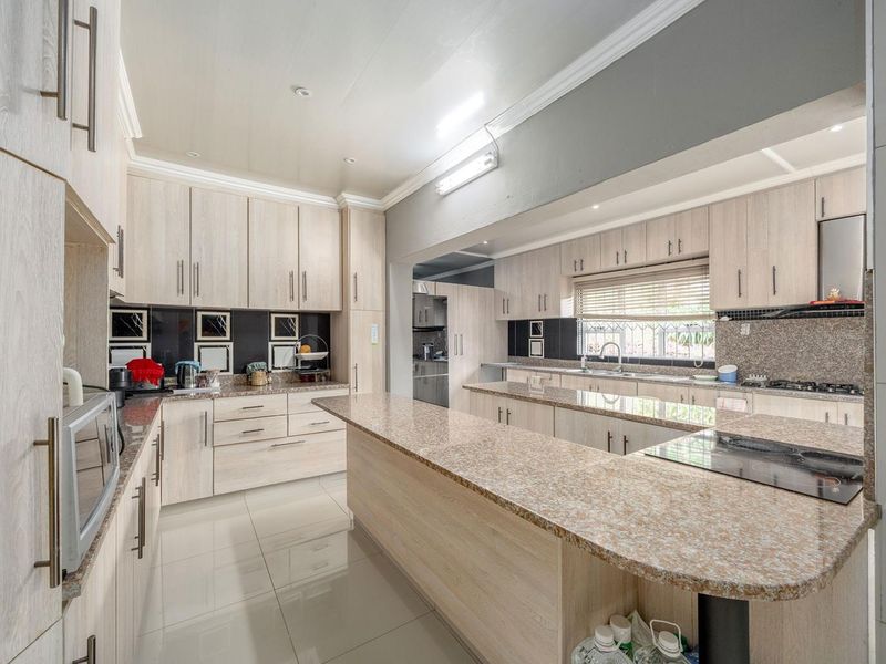 Spacious kitchen featuring light wood-finish cabinetry, granite countertops, a central breakfast island, and integrated cooking appliances with tiled flooring throughout.