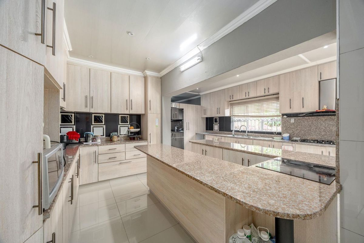Spacious kitchen featuring light wood-finish cabinetry, granite countertops, a central breakfast island, and integrated cooking appliances with tiled flooring throughout.