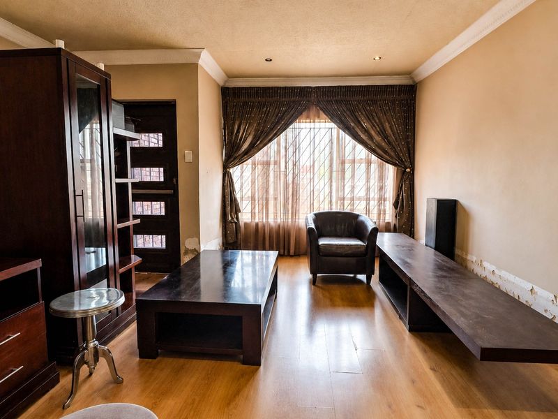 A living room featuring laminate flooring, coved ceilings, and recessed lighting, currently showing signs of wall surface damage requiring repair.
