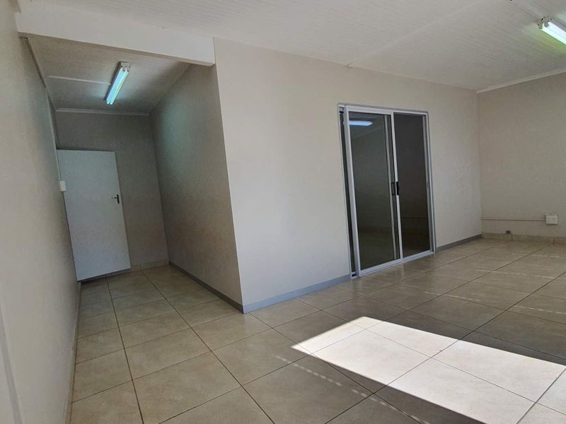 A bright, empty office space featuring neutral tiled flooring, fluorescent lighting, and a sliding glass door leading to an adjacent area.