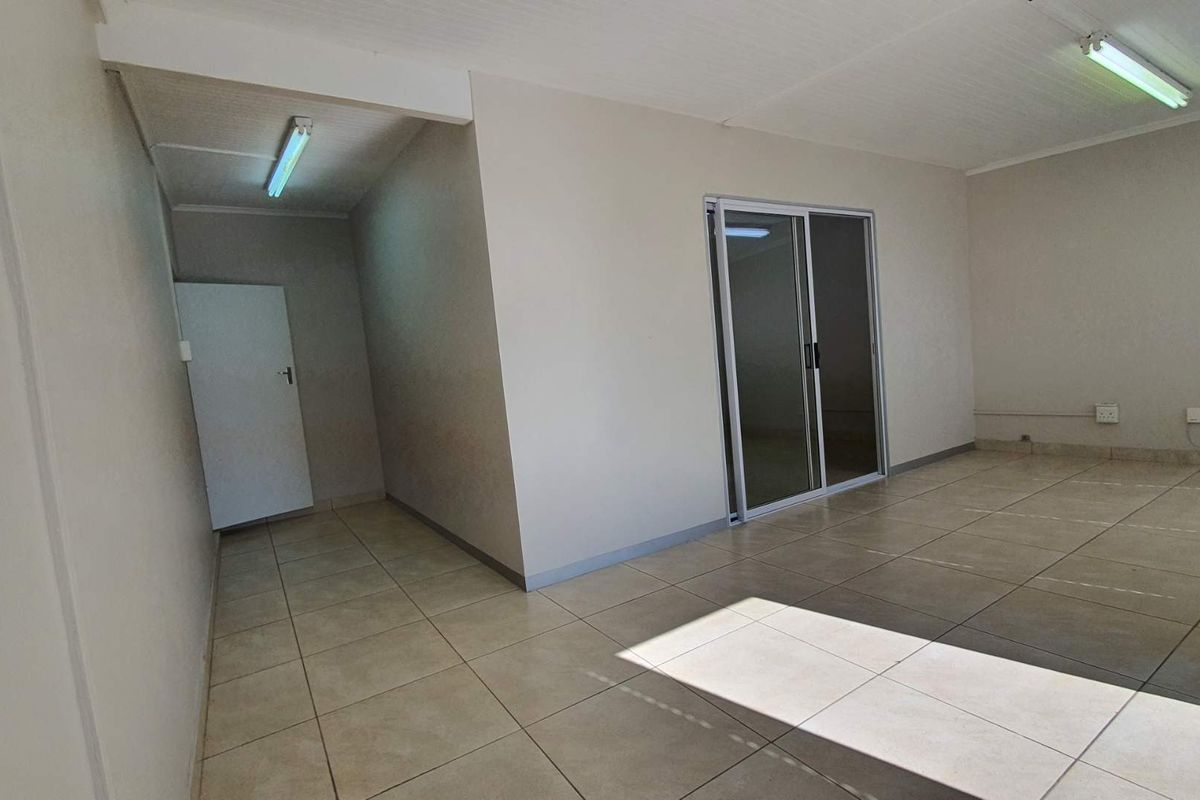 A bright, empty office space featuring neutral tiled flooring, fluorescent lighting, and a sliding glass door leading to an adjacent area.