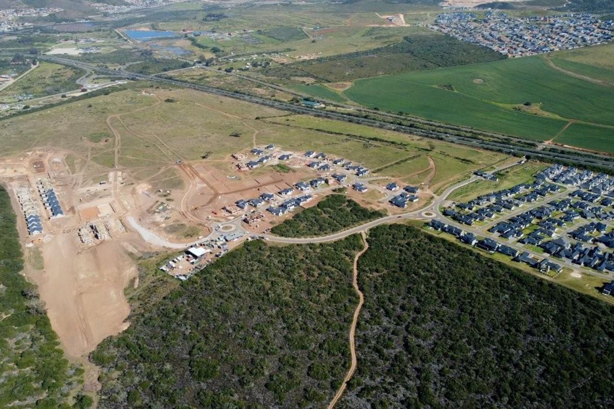 Aerial view of a residential development site showing ongoing construction, road infrastructure, and surrounding natural landscape.
