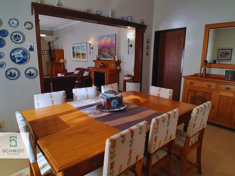A traditional dining room featuring a wooden fireplace mantel and an open archway leading into the adjacent living area.