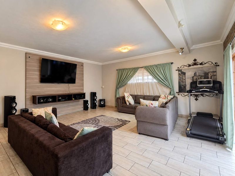 Spacious living room featuring tiled flooring, a modern built-in media wall unit, and recessed ceiling lighting, offering a comfortable and functional living space.