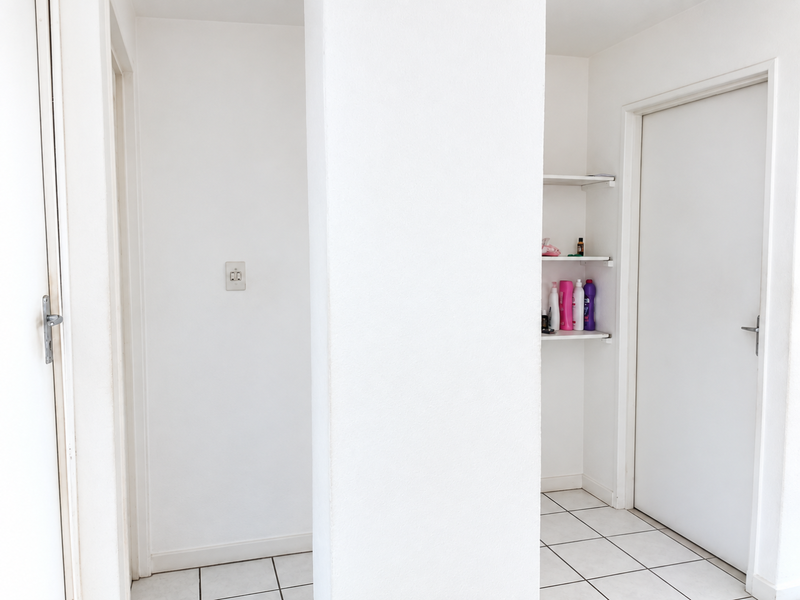 A clean, neutral hallway featuring tiled flooring, built-in shelving, and internal doors, providing a functional transition space within the apartment.