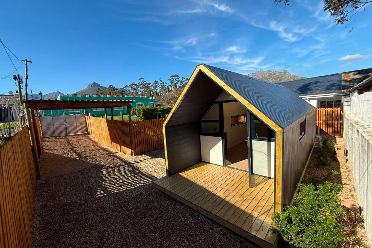 A modern detached cottage structure featuring a timber deck, corrugated metal roof, and surrounding timber fencing in a well-maintained rear garden setting.
