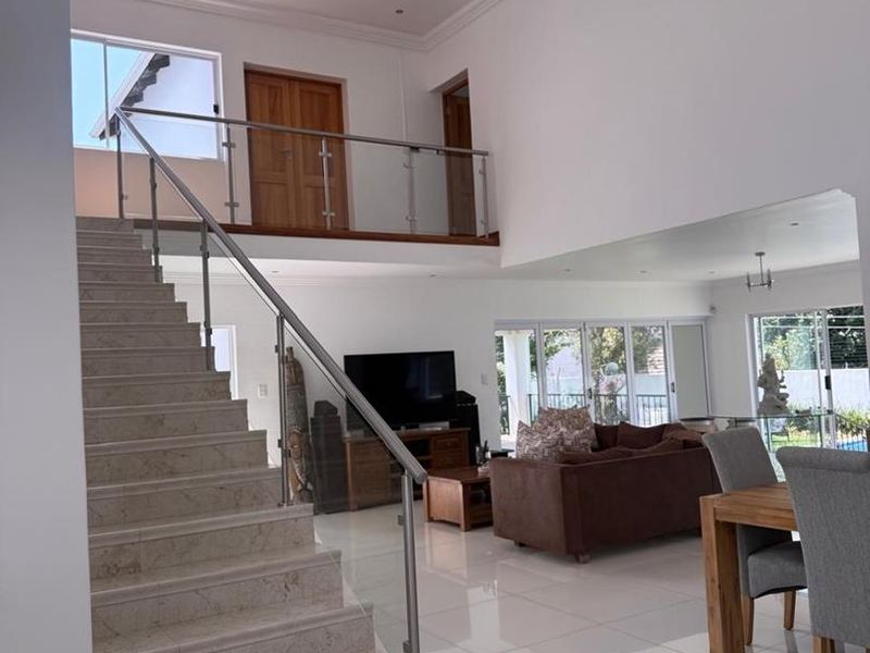 Spacious open-plan living area featuring a grand stone staircase with glass balustrade, high ceilings, and large sliding doors leading to the outdoor space.