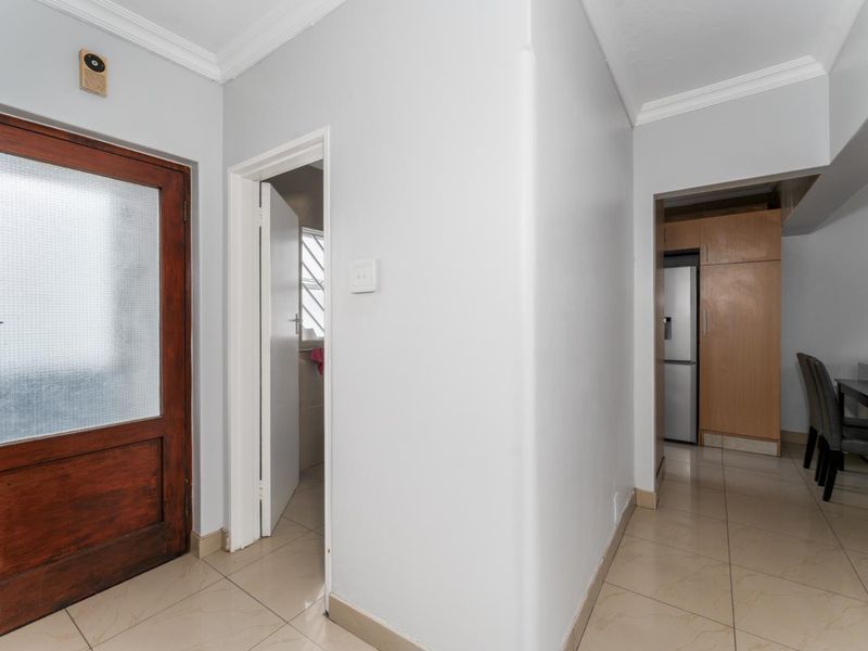 A functional hallway area featuring tiled flooring, crown molding, and a solid timber entrance door, providing access to adjacent living and utility spaces.