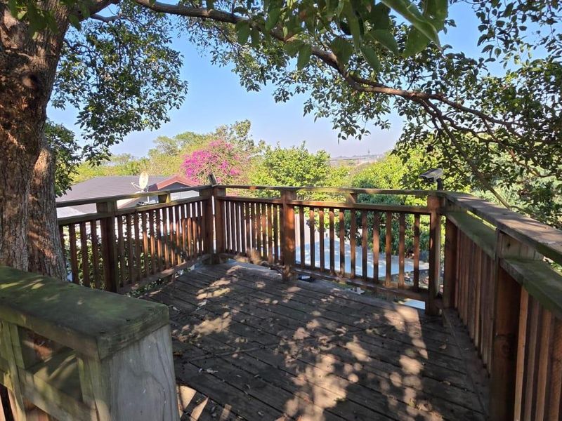An elevated wooden balcony or deck area featuring timber railings and mature tree integration, offering an open outdoor space.
