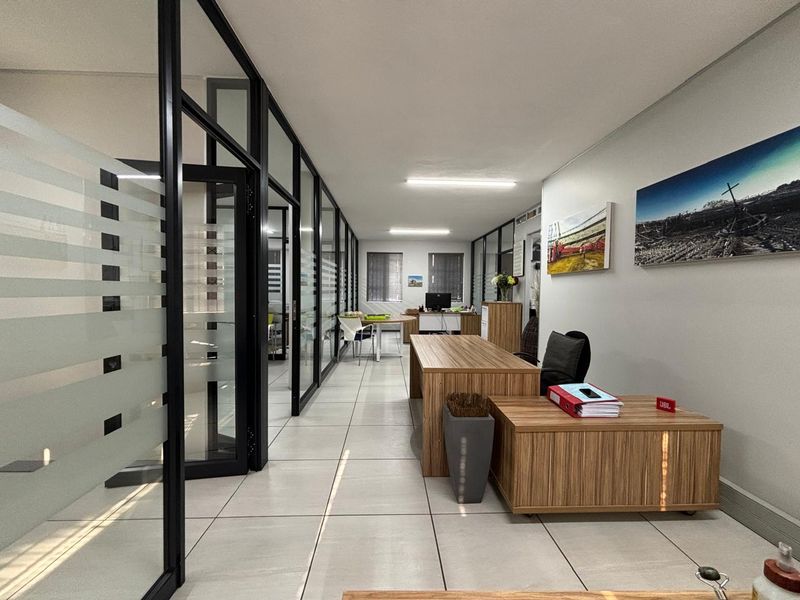 Modern office space featuring glass partition walls with black aluminium frames and clean tiled flooring, providing a professional and bright work environment.