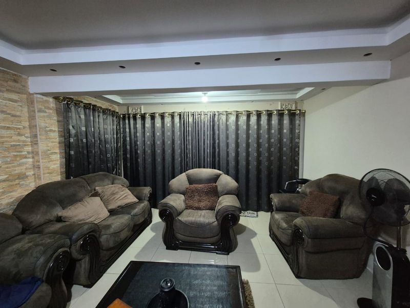 A living room featuring a stone veneer accent wall, tiled flooring, and a dropped ceiling bulkhead with recessed lighting.