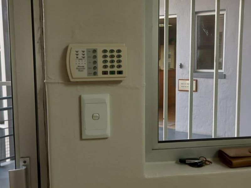 Interior view of an office space featuring a security alarm keypad, light switch, and security bars on the window.