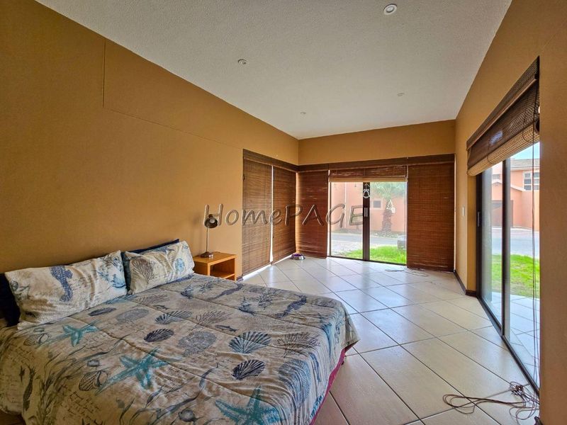 Spacious bedroom featuring large sliding glass doors with bamboo blinds, tiled flooring, and recessed ceiling lighting, offering direct access to the exterior.